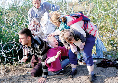 أحد العائلات النازحة أثناء عبورها السياج الشائك من صربيا إلى المجر